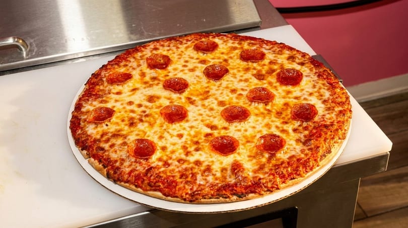 Whole pepperoni pizza with melted, bubbly cheese on a white counter.