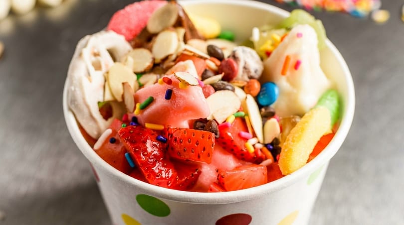 Colorful frozen dessert in a polka-dot cup with strawberries, sprinkles, almonds, and candies.